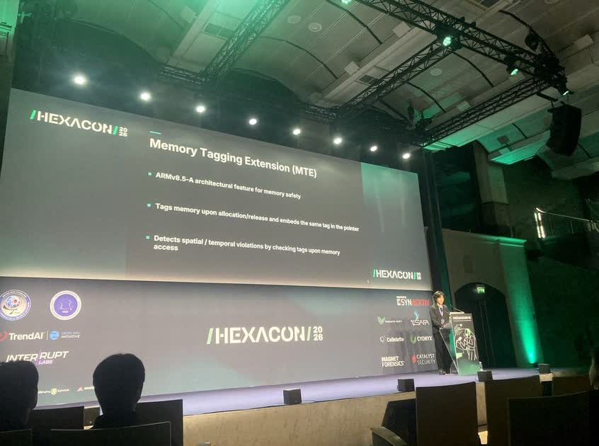 Hexacon 2026 舞台上，講者站在講台旁，大屏幕顯示 Memory Tagging Extension (MTE) 的投影片